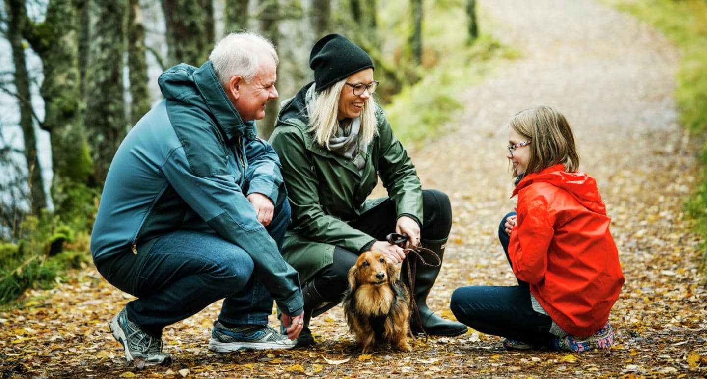 Bedstefar og mor sidder med datter på sti i skoven